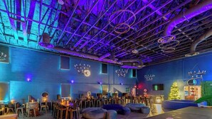 An indoor space with a high ceiling, exposed beams, and hanging circular light fixtures. There are seating areas with tables and chairs, and a Christmas tree in the background. - Treehouse & Theater Arcade at Rock Spring Resort (Rock Spring)