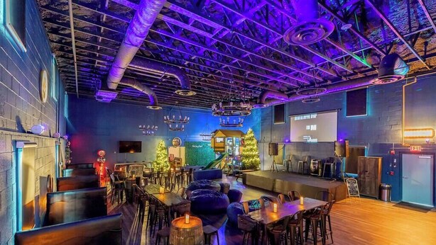 A bar area with wooden tables and stools, a stage with a Christmas tree, and a neon exit sign. - Treehouse & Theater Arcade at Rock Spring Resort (Rock Spring)