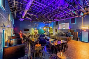A bar area with wooden tables and stools, a stage with a Christmas tree, and a neon exit sign.