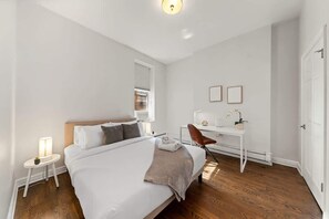Ein modernes Schlafzimmer mit einem großen Bett, Nachttischen, einem Schreibtisch und einem Sessel.