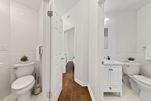 Ein Badezimmer mit weißen Sanitärobjekten, Holzboden und einem Flur, der zu einem anderen Raum führt.