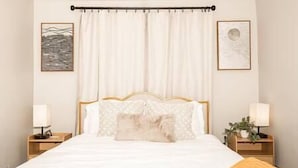 Ein ordentlich eingerichtetes Schlafzimmer mit einem großen Bett, zwei Nachttischen mit Lampen und einem Vorhang.