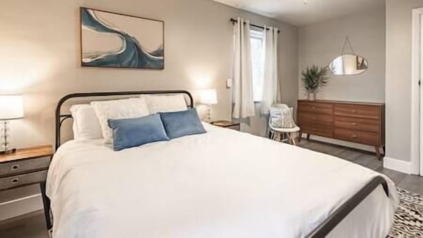 Un dormitorio con cama, mesitas de noche, cómoda, ventilador de techo y un cuadro en la pared.
