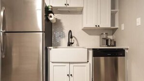 Una cocina compacta con refrigerador de acero inoxidable, lavavajillas y muebles blancos.