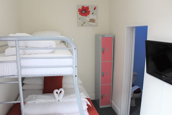 A bunk bed with white bedding and a red pillow, a pink cabinet, and a television on a white cabinet. - Backpackers Hotel (Blackpool)