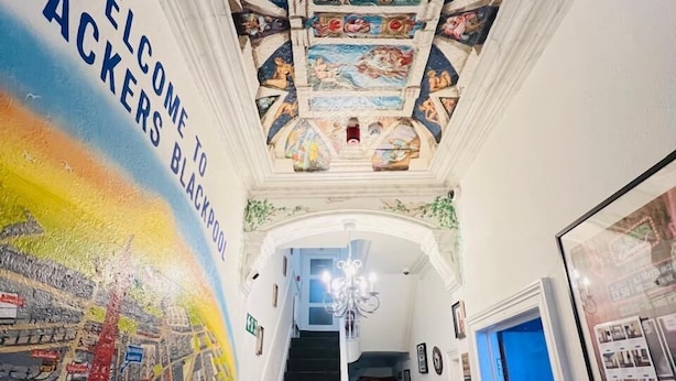 Un couloir orné d’une fresque représentant un paysage urbain, un escalier et un plafond décoré d’œuvres d’art classiques.