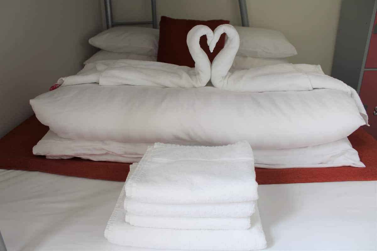 Un lit bien fait, avec du linge de lit blanc et une serviette pliée en forme de cœur.
