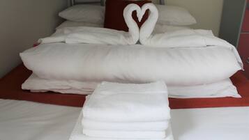 Una cama bien hecha con sábanas blancas y una disposición de toallas en forma de corazón.