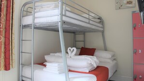 Un lit superposé avec une literie blanche et un oreiller rouge, une échelle en métal et un rideau rouge.