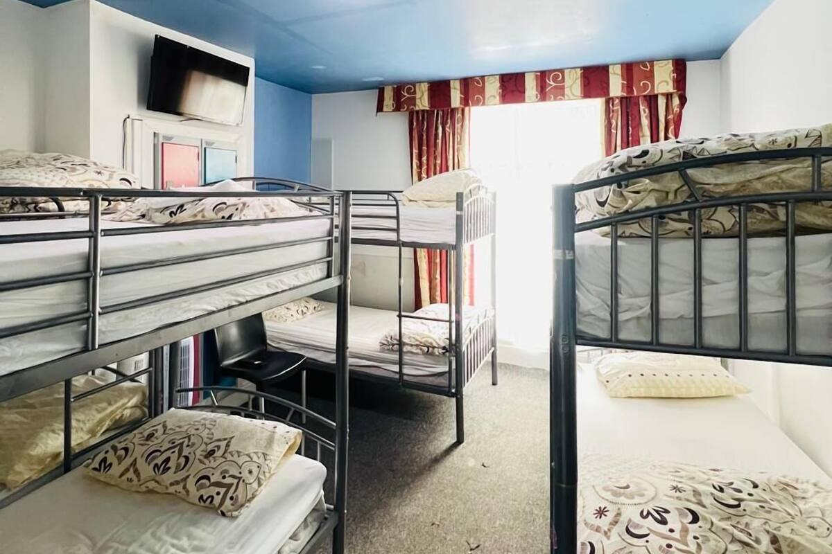 Une chambre de dortoir avec des lits superposés, un téléviseur accroché au mur et une fenêtre avec des rideaux.