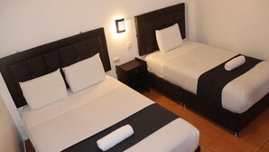 A hotel room with two single beds, each with a dark headboard and white bedding. There is a small bedside table with a lamp between the beds. - BackpackerKilla (Machu Picchu)