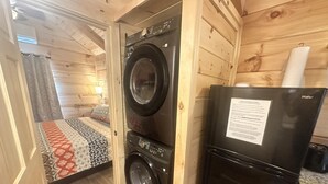 Une pièce de taille modeste équipée d’un lave-linge, d’un réfrigérateur et d’un lit avec une literie à motifs.