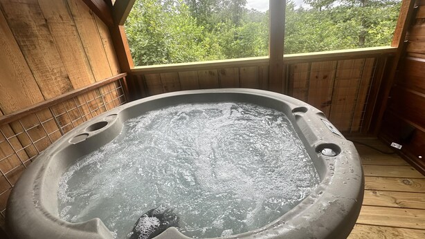 Un bain à remous à l’intérieur d’un chalet en bois, avec vue sur les arbres.