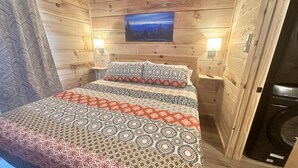 Une chambre confortable avec une couvre-lit à motifs, un tableau au-dessus du lit et des murs en bois.