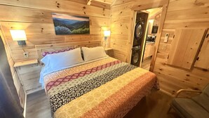 A wooden cabin bedroom with a bed, a painting, and a washing machine visible through an open door. - Hideaway Holler - Hot Tub, Fireplace, Wi-Fi (Union Mills)