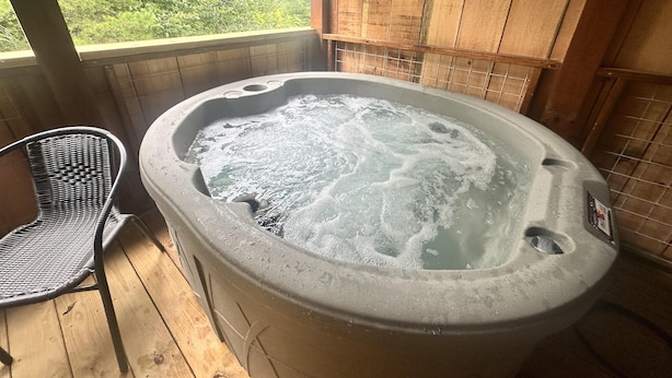 A hot tub with a wooden deck and a wicker chair. - Hideaway Holler - Hot Tub, Fireplace, Wi-Fi (Union Mills)