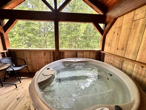A hot tub in a wooden cabin with a view of trees.