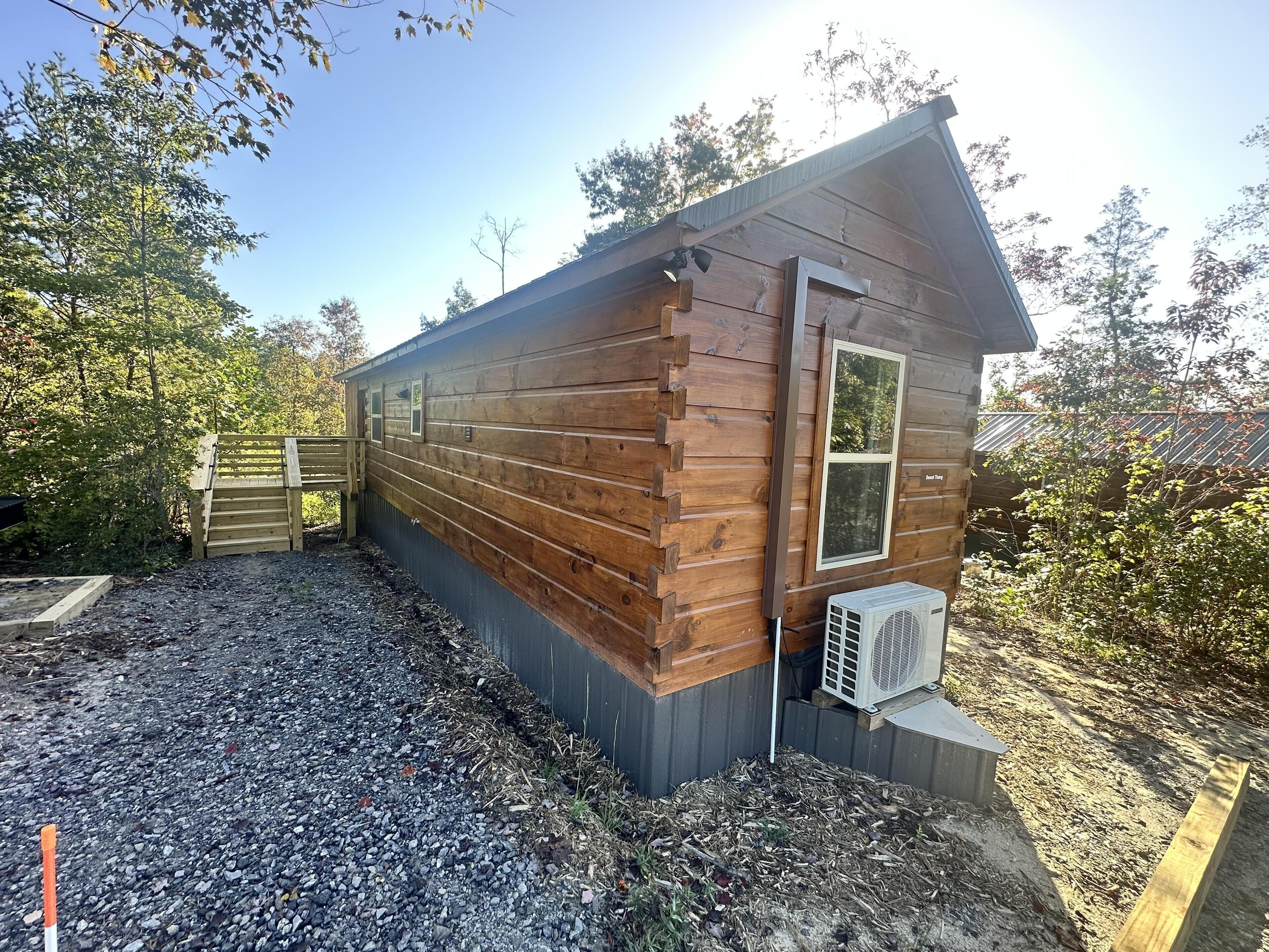 Una baita di legno con un piccolo garage annesso, un vialetto sterrato e una recinzione in metallo.