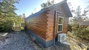 A wooden cabin with a small attached garage, a gravel driveway, and a metal fence.