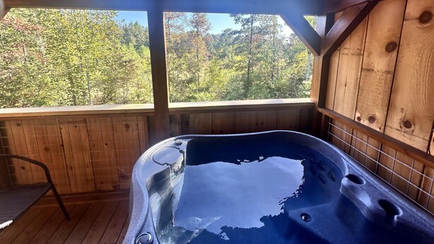 A wooden cabin with a hot tub and a view of a forest.