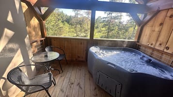 A wooden deck with a hot tub, a round table, and two chairs.