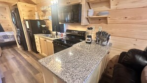 A compact kitchen with granite countertops, wooden cabinets, a black refrigerator, a microwave, and a stove.