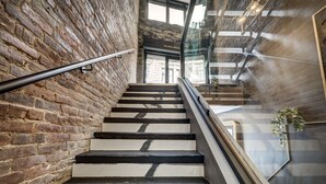 Una scala con un lato adiacente a un muro in mattoni e l'altro con ringhiera in vetro, che conduce a un piano superiore.