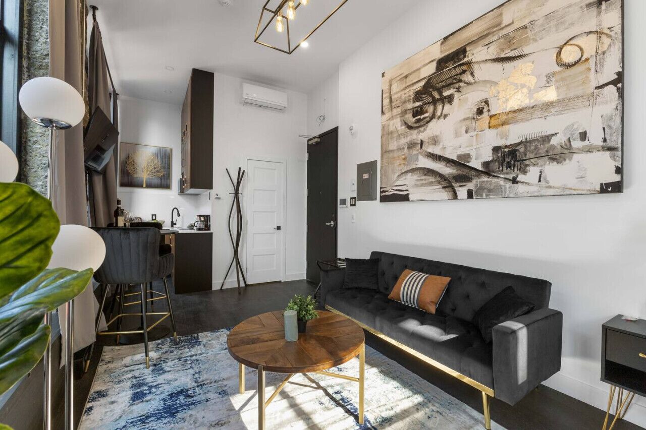 A modern living room with a black sofa, a round coffee table, and a large abstract painting on the wall.