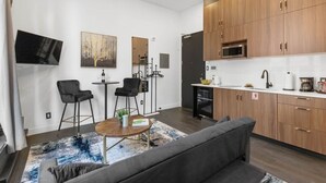 A modern kitchen with wooden cabinets, a microwave, and a sink. There is a dining area with two chairs and a small table. - Old Montreal Corner, Loft, 10 feet ceilings, 1 Bed (Montréal)