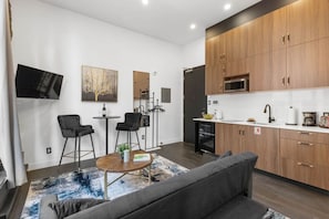 A modern kitchen with wooden cabinets, a microwave, and a sink. There is a dining area with two chairs and a small table. - Old Montreal Corner, Loft, 10 feet ceilings, 1 Bed (Montréal)