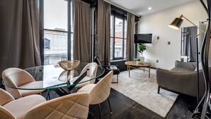 Una sala de estar moderna con una mesa de comedor de vidrio, sillas de cuero, un sofá y un televisor.