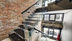 Una escalera con barandas de cristal, un muro de ladrillo y un panel de piedra decorativo.
