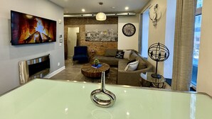 A modern living room with a fireplace, a television, and a cityscape painting.