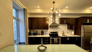A modern kitchen with dark wooden cabinets, stainless steel appliances, and a glass-top dining table.