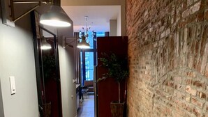 A hallway with a wooden floor, a brick wall, and a large mirror on the left.