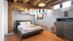 A bedroom with a bed, wooden ceiling beams, a dresser, and a picture on the wall.