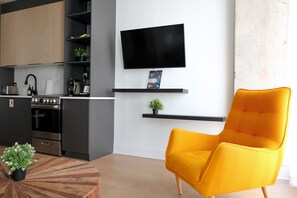 A modern kitchen with a built-in oven, a flat-screen TV mounted on the wall, and a bright yellow armchair in a living area.