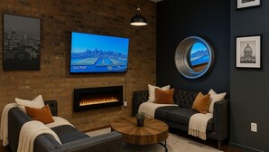 Un salon moderne avec un mur en briques, un téléviseur à écran plat, une cheminée, deux canapés et une table basse ronde.