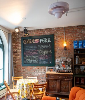 Een gezellig café interieur met een krijtbordmenu, bakstenen muur, houten meubels en koffiezetapparatuur.