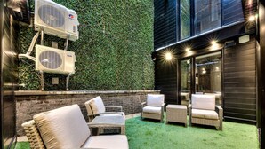 Un espace extérieur aménagé avec du gazon synthétique, des meubles en osier et deux unités de climatisation.