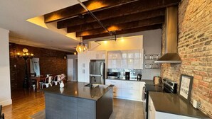 A modern kitchen with a central island, white cabinetry, and a brick wall. - Stunning 2BR - Old Montreal (Montréal)