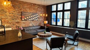 A modern living room with a brick wall, a large window, a sofa, a coffee table, and a dining area. - Stunning 2BR - Old Montreal (Montréal)