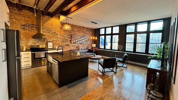 A modern kitchen with a large island, exposed brick walls, and large windows providing natural light. - Stunning 2BR - Old Montreal (Montréal)