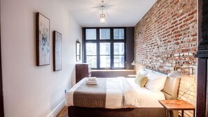 A modern bedroom with a brick wall, a large window, a bed with a headboard, and a bedside table. - Stunning 2BR - Old Montreal (Montréal)