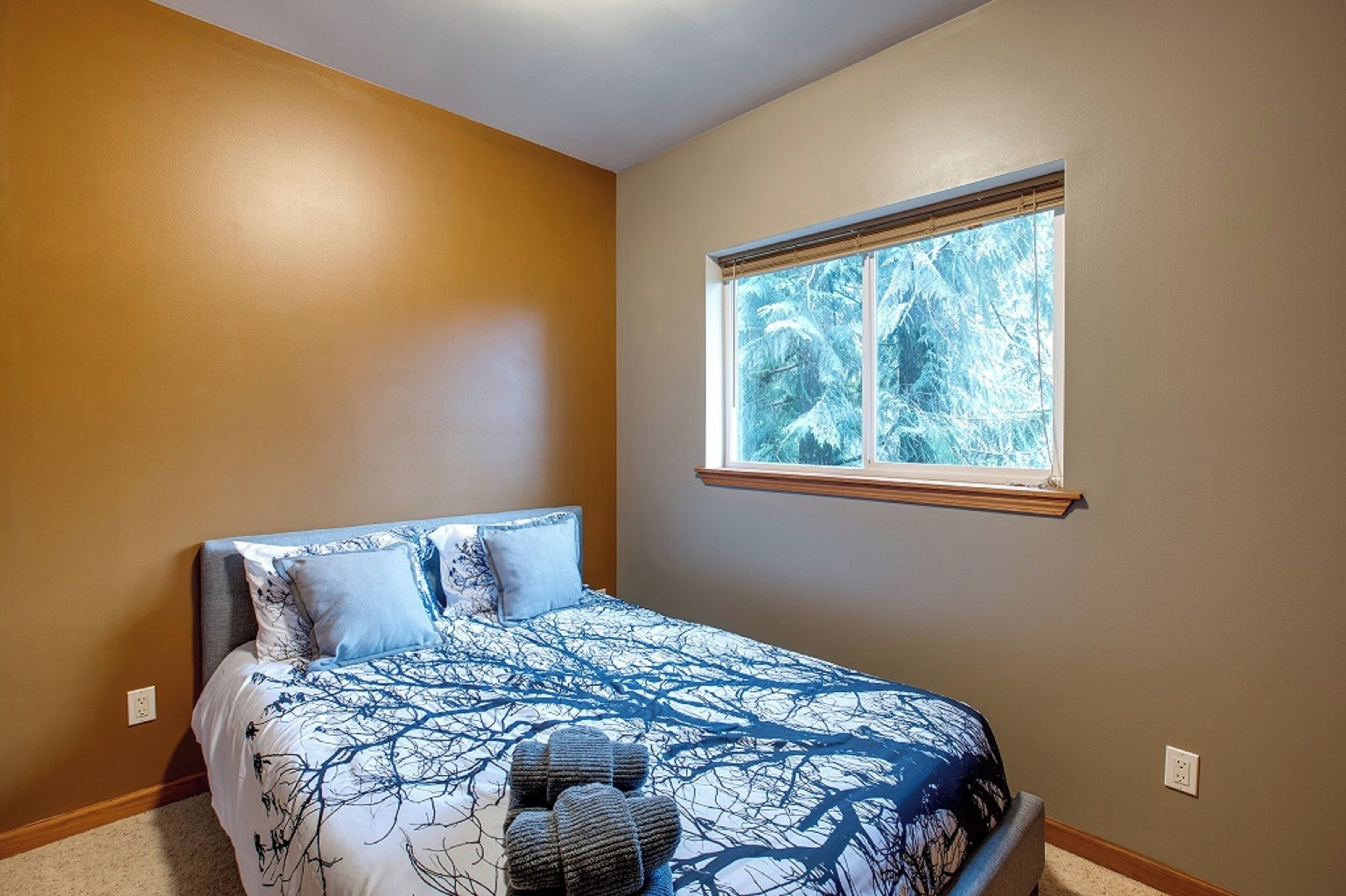 Un dormitorio con cama, ventana y vista a árboles.