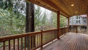 Une terrasse en bois dotée d’une rambarde, qui offre une vue sur une zone boisée avec de grands arbres.