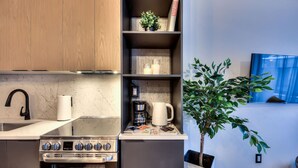 Eine kleine Küche mit Herd, Backofen und Spüle, einer Kaffeemaschine und einem Blumentopf.