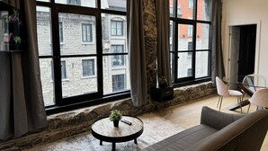 A modern living room with a large window, stone wall, and a round coffee table with a plant. - Luxury 2BD Loft-Old Montreal-2B (Montréal)