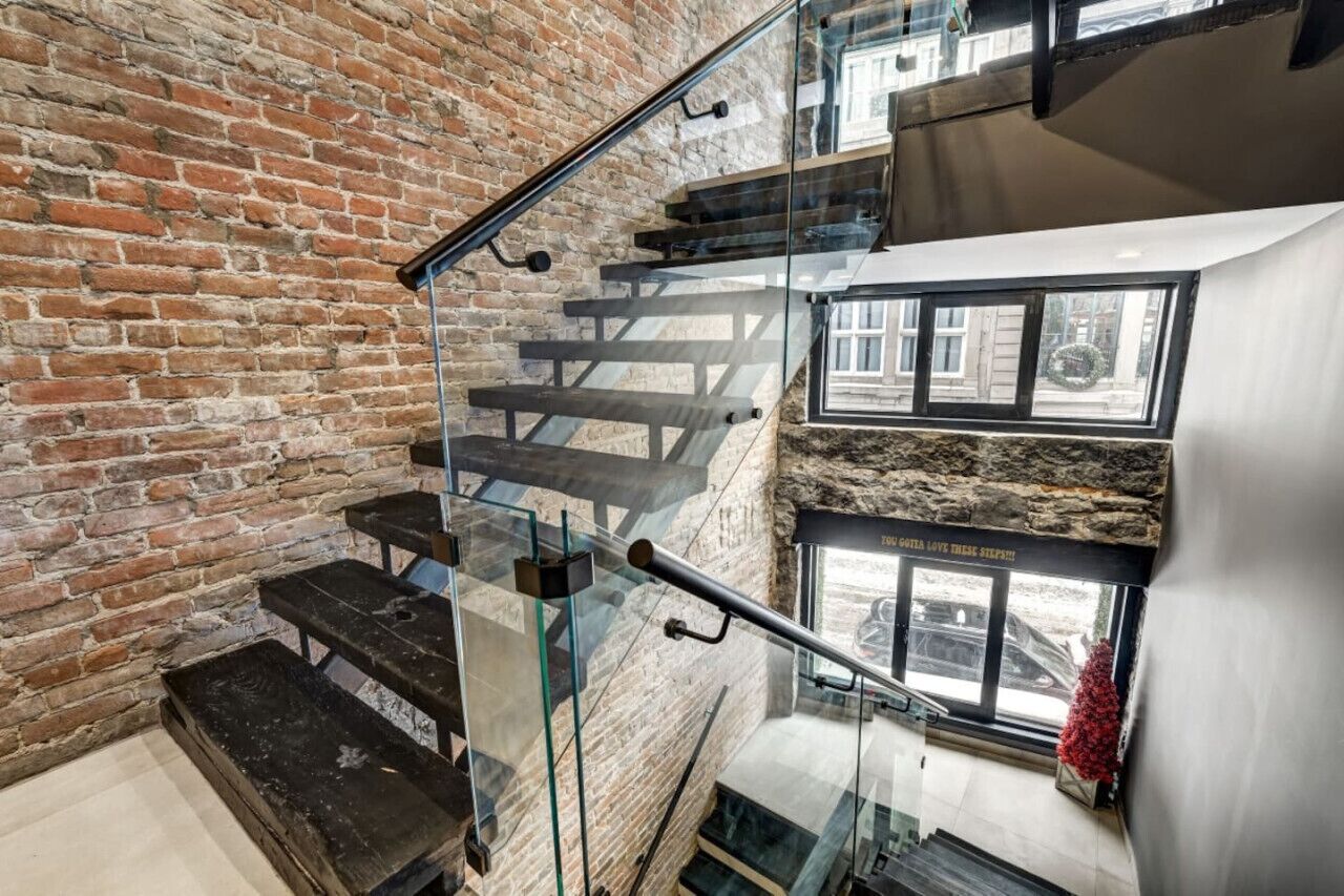 Una escalera con barandillas de vidrio y pared de ladrillo.