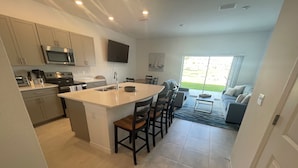 Een moderne keuken met een centraal eiland, een eetgedeelte met stoelen en een woonkamer met een bank en uitzicht op de omgeving.